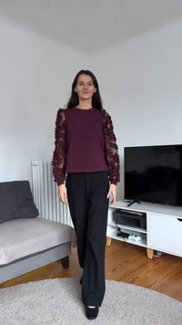 Haut bordeaux avec manches en dentelle transparente texturée, associé à un pantalon noir à jambes larges. Tissu lisse, coupe ajustée et décolleté simple.