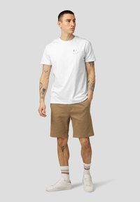 Hvit bomullst-skjorte med et lite grått smilefjes, kombinert med brune shorts og hvite sneakers, med stripete ankelsokker.