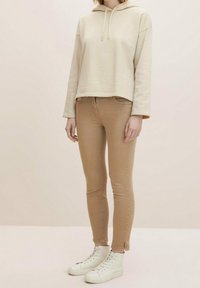 Sudadera corta beige con cordones, combinada con jeans ajustados marrón claro y zapatillas altas blancas. Texturas suaves y diseño ajustado.