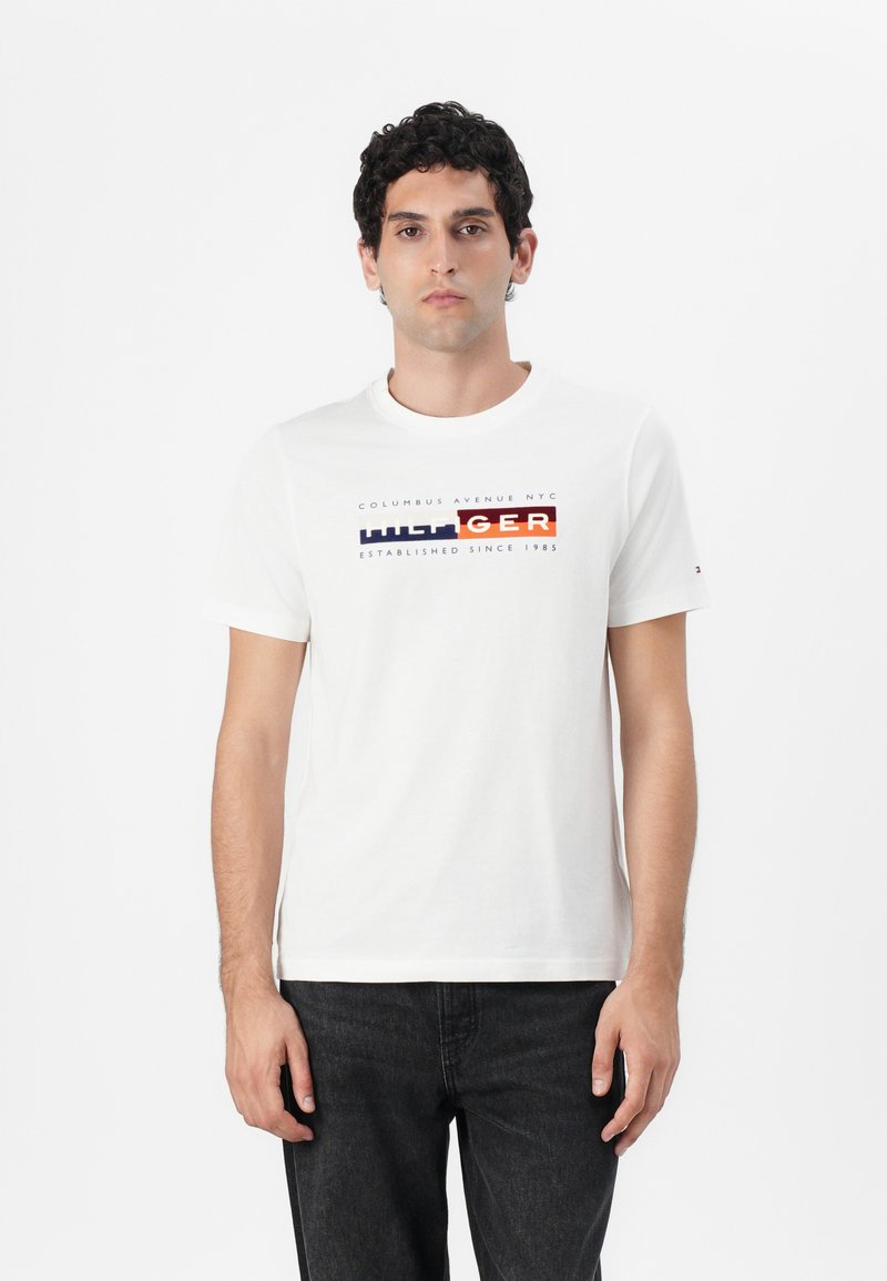 White cotton t-shirt with short sleeves featuring a colorful "TOMMY HILFIGER" logo design across the chest. Standard crew neckline.