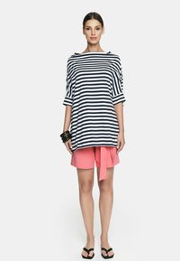 Niebiesko-biała w pasy oversize'owa bluzka zestawiona z różowymi szortami. Bluzka ma szeroki dekolt i krótkie rękawy; szorty posiadają wiązany detal.