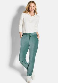 Lichte, lang-sleeve crème polo shirt gecombineerd met losse, teal joggers met een taillekoord en zijzakken, gedragen met witte sneakers.