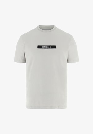Lichtgrijs katoenen T-shirt met een ronde hals en korte mouwen, voorzien van een zwart rechthoekig label met het "GUESS EST. 1981" logo in witte letters.
