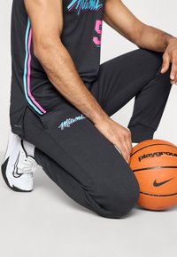 Čierny atletický dres a nohavice s farebnou grafikou "Miami". V zábere sú aj basketbalová lopta a biele tenisky. Tkanina vyzerá hladko a priedušne.