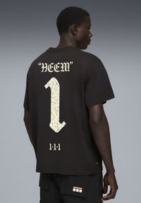 Sort bomulds t-shirt med et stort hvidt grafisk design på ryggen, der viser "NEEM" og et fedt tal "1" i et plettet design, nedenunder tre lodrette linjer.