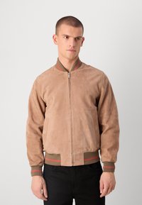 Türkisfarbener Wildleder-Bomberjacke mit einem frontalen Reißverschluss, gerippten braunen und grünen Streifen an den Ärmelbündchen sowie seitlichen Taschen. Glatte Textur und lockere Passform.