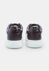 Tumepruunist nahast sneakers paar, millel on pressitud muster ja valged tallad, nähtud tagant lihtsal taustal.