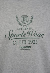 Camiseta de algodón gris con texto impreso en verde: "AUTHENTIC SportsWear CLUB 1923" y "hummel SPORTSWEAR" con un diseño decorativo de laurel.