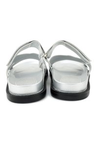 Pair of silver open-toe sandals with adjustable straps and black soles, shown from the rear on a white background.