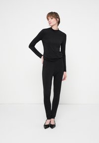 Čierny priliehavý top s dlhými rukávmi a zodpovedajúce legíny, zdobené rozptýlenými striebornými bodkami. Modelka má na sebe čierne špicaté baleríny.