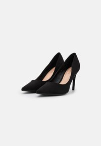 Zapatos de tacón alto de ante negro con puntera afilada, textura suave y tacón delgado, con un forro interior sutil de color beige claro.