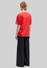 Rotes Baumwoll-T-Shirt mit lockerer Passform, rundem Ausschnitt und kurzen Ärmeln, kombiniert mit weiten schwarzen Hosen. Die Rückansicht zeigt minimale Details.