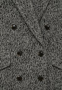 Černobílý kabát s rybí kostí, dvouřadý se černými knoflíky a klopovými kapsami.