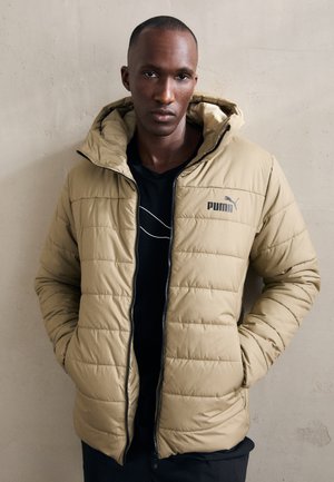 Giacca a vento beige con zip, cappuccio e design trapuntato. Presenta un logo Puma nero sul petto sinistro e polsini a costine.