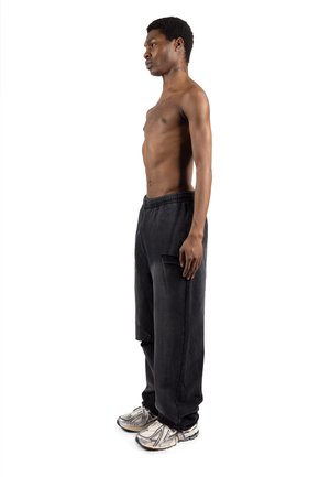 Pantalones jogger negros de corte holgado con cintura elástica y bolsillo lateral. Combinados con zapatillas grises y blancas. Modelo mostrado de perfil.