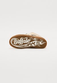 Tênis Buffalo com parte superior em tom de beje, acentos em preto e sola de borracha castanha. Design notável de chamas brancas e logótipo na sola.