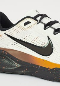 Sport shoes with a mesh upper in white, featuring a black swoosh and orange accents. The sole is black with orange and brown speckles.