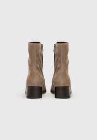 Paire de bottines en daim taupe avec talons blocs empilés et fermetures éclair à l'arrière, vues de dos sur fond blanc.