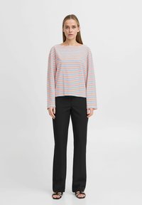 Haut à manches longues rayé en rouge, bleu et blanc, associé à un pantalon droit noir. Les sandales présentent un design à lanières.