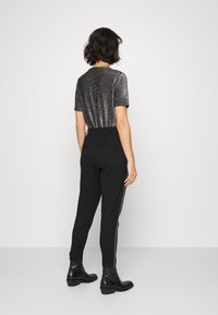 Czarne spodnie dresowe z bocznymi paskami, w połączeniu z krótkim, metalicznie srebrnym topem o okrągłym dekolcie. Tkanina o fakturze, luźny krój.