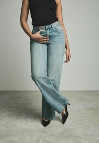 Lichtblauwe straight-leg jeans met een hoge taille en een vijf-pocket ontwerp, gecombineerd met een zwart mouwloos topje en pointed zwarte hakken.