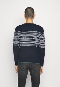 Granatowy sweter z białym geometrycznym wzorem na górnej części pleców. Długie rękawy, ściągacze na rękawach i brzegu, dzianinowa faktura.