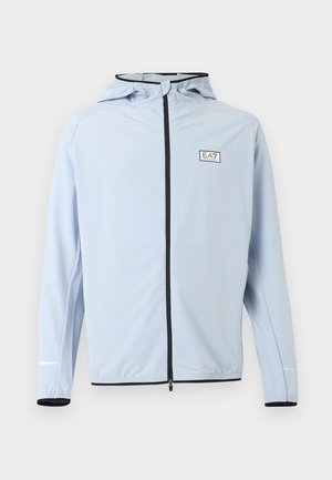 Gaiši zils pilnībā aizslēdzams kapuciņmētelis ar melnu rāvējslēdzēja apdari un EA7 Emporio Armani logotipu krūtīs, elastīgiem aprocēm un atstarojošām piedurkņu detaļām.