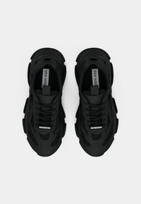 Chaussures de sport noires avec un design en mesh et en caoutchouc, présentant des accents rembourrés, des semelles épaisses et des lacets, mettant en avant une surface texturée.