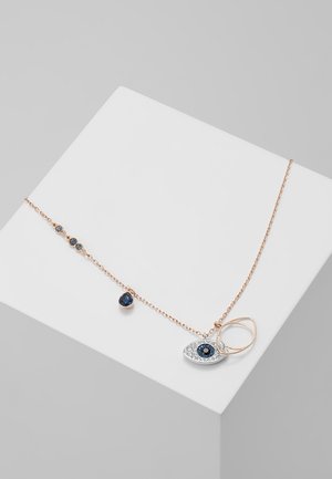 Collier chaîne en or rose avec des gouttes de pierres précieuses bleues et un pendentif en forme d'œil décoré de pierres bleues et blanches sur un socle blanc.