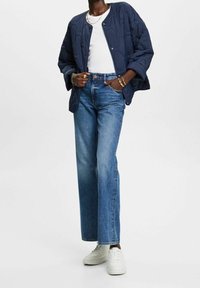 Giacca bomber trapuntata blu navy con bottoni a pressione, t-shirt bianca, jeans azzurri a vita alta e sneakers bianche. Design semplice, vestibilità rilassata.
