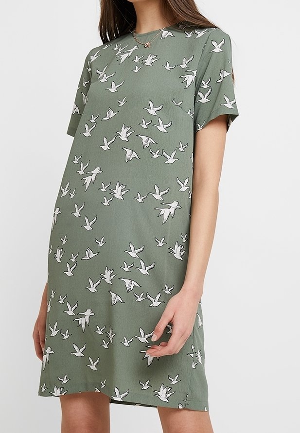 Kurzärmliges grünes Kleid mit lockerer Passform, das durchgehende weiße Vogelmuster aufweist. Weicher Stoff, runder Ausschnitt und seitliche Taschen.
