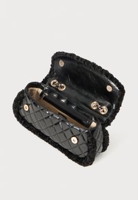 Borsa a tracolla nera trapuntata con bordo in pelliccia nera morbida, dotata di hardware in tono oro e una tasca interna con zip, aperta per mostrare lo spazio di archiviazione.
