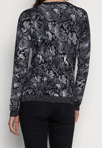 Pull à manches longues noir et blanc avec un motif serpent, tissu texturé et une ceinture accentuée de métal.