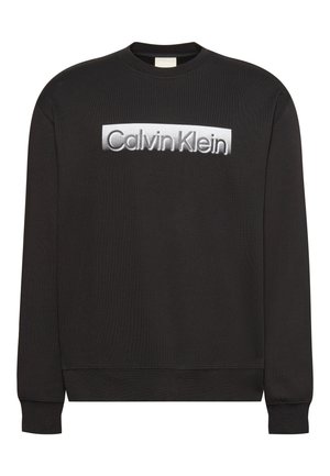 Sweat-shirt noir à manches longues avec le logo « Calvin Klein » blanc centré sur la poitrine, doté de poignets et d’un ourlet côtelés.