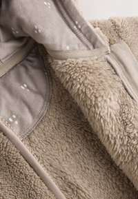 Tissu polaire beige avec une surface texturée et duveteuse ; présente une doublure intérieure lisse et à motifs ainsi qu'un bord contrastant le long des bords.