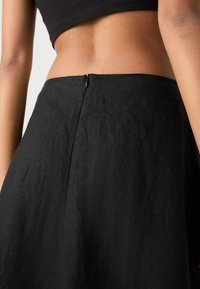 Sort linned skirt med en glat tekstur, subtil glans og en lynlåslukning bagpå med en krog, designet med en flydende silhuet.