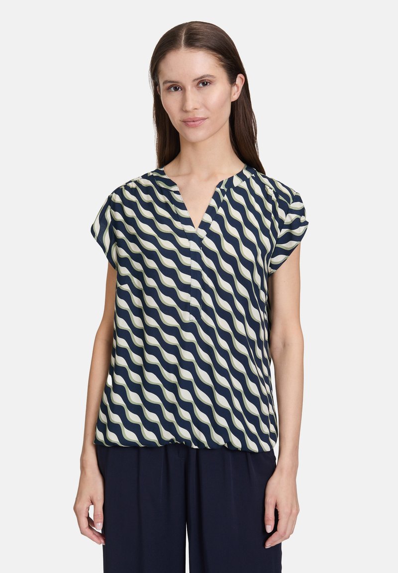 Granatowa i kremowa bluzka z falistym wzorem, z krótkimi rękawami i dekoltem w serek. Lekki materiał o luźnym kroju, idealna na codzienne noszenie.
