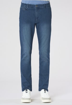 Jeans blu slim fit da uomo in denim indossati con sneakers bianche su sfondo semplice.