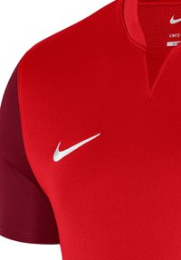 Maglietta Nike Dri-FIT rossa con un logo bianco ben visibile. Presenta un colletto testurizzato e maniche di un rosso scuro a contrasto. Tessuto liscio e traspirante.
