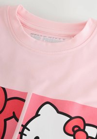 T-shirt di cotone rosa con design di Hello Kitty, con contorni neri e dettagli rossi. La maglietta ha un collo rotondo e maniche corte.