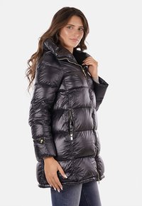 Giubbotto imbottito nero con colletto alto, chiusura a zip e tasche laterali. Presenta una texture liscia e lucida con sottili accenti in hardware dorato.