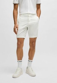 White cotton shorts with a zipper and button closure, flat front, side pockets, and rolled cuffs, paired with a white polo and light sneakers.