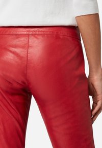Rode leren broek met een gladde textuur en een aansluitend ontwerp, voorzien van een hoge tailleband en subtiele naden langs de achterkant voor extra detail.