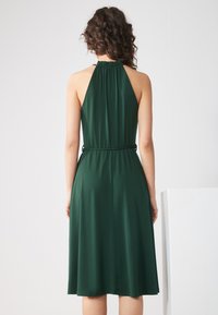 Green halter neck dress with a gathered neckline, cinched waist, and flowing skirt. Made from soft, smooth fabric with a subtle sheen.