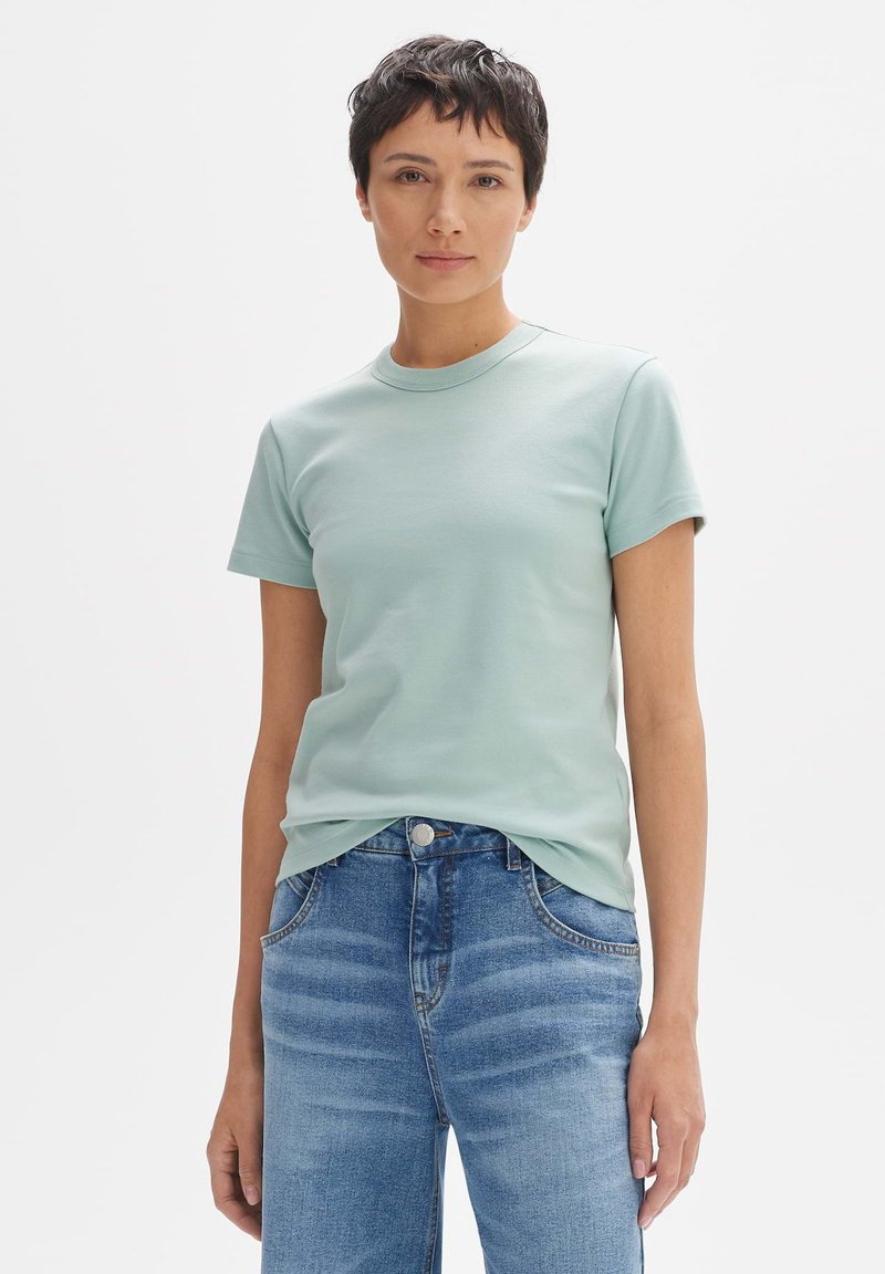 T-shirt verde menta, maniche corte, scollatura rotonda, materiale in cotone morbido. Indossato con jeans blu in denim con un lavaggio chiaro e un leggero sbiadimento.
