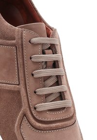 Chaussure en daim marron avec une surface texturée, présentant des lacets plats tissés, une languette rembourrée et des coutures contrastantes le long des bords.