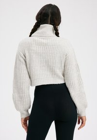 Cremefarbener gerippter Strickpullover mit hohem Kragen und Ballonärmeln, kombiniert mit schwarzen gerippten Leggings. Kurzes Design mit strukturierten Details.
