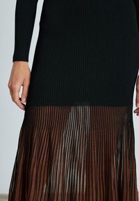 Abito nero a coste con gonna plissettata trasparente marrone. Il design passa dal nero nella parte superiore a una parte inferiore marrone textured.