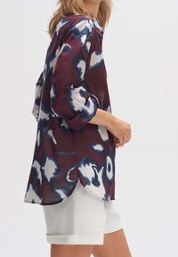 Chemise maroon et blanche à motifs avec des accents bleus, tissu léger, coupe décontractée, manches longues retroussées aux poignets, ourlet arrondi.