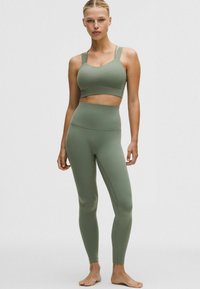 Brassière de sport vert olive et leggings taille haute en tissu lisse et extensible. Caractéristiques : larges bretelles, design sans coutures, silhouette ajustée.